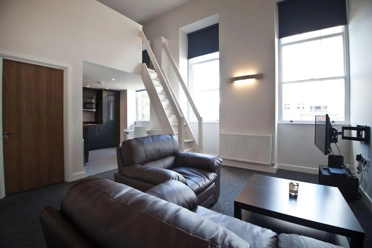 Leather sofas stairs kitchen and windows living room at Dean Clarke Lofts in Exeter Student Accommodation