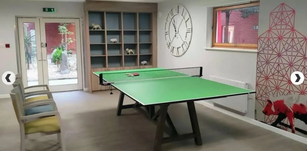 Ping pong table chairs bookshelf clock living room at Lilian Knowles House in London Student Accommodation