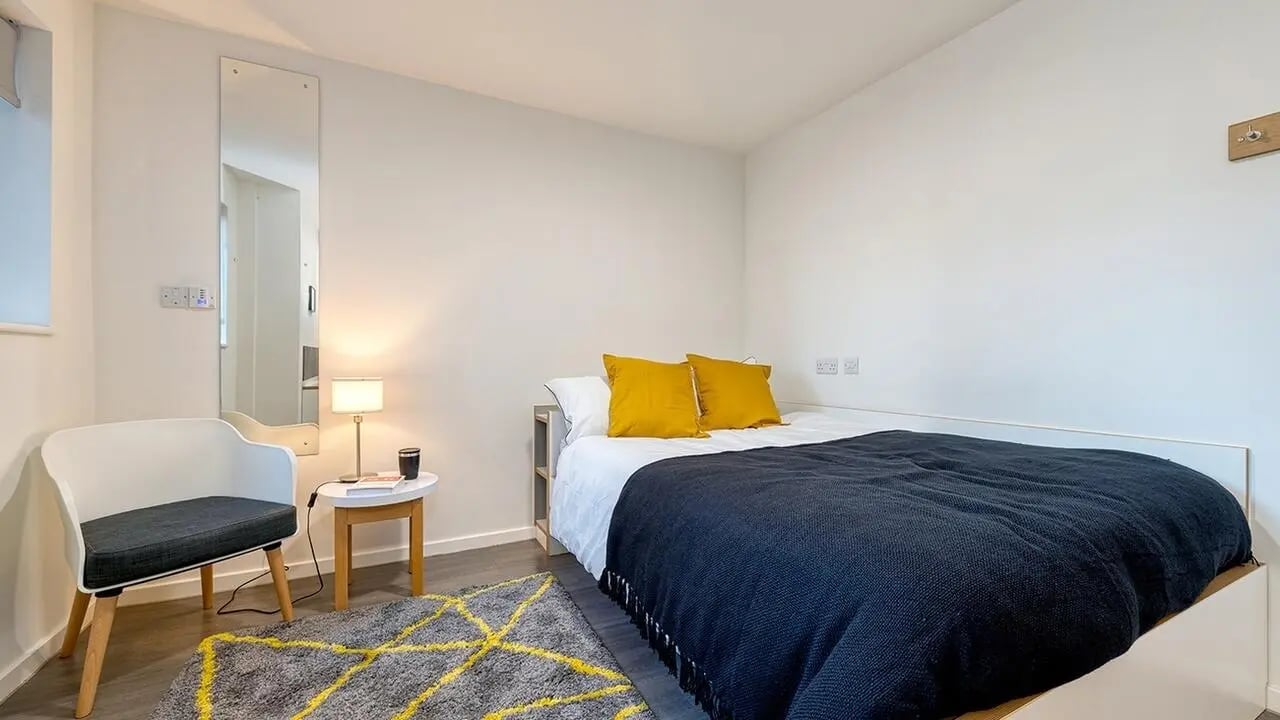 Bed with yellow pillows and dark blue blanket bedroom at Collegiate Merlin Heights in Leicester Student Accommodation