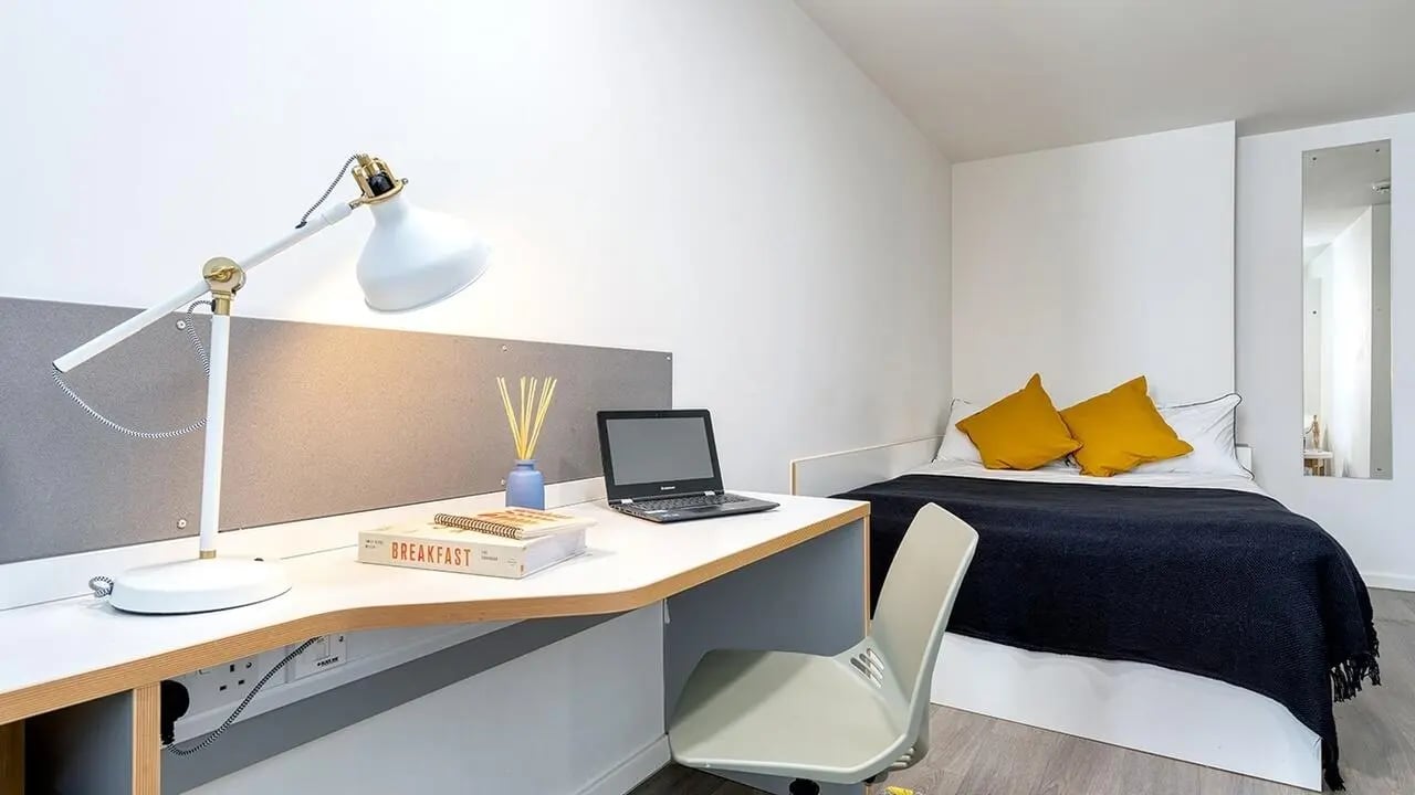 Desk lamp laptop bed yellow pillows bedroom at Collegiate Merlin Heights in Leicester Student Accommodation