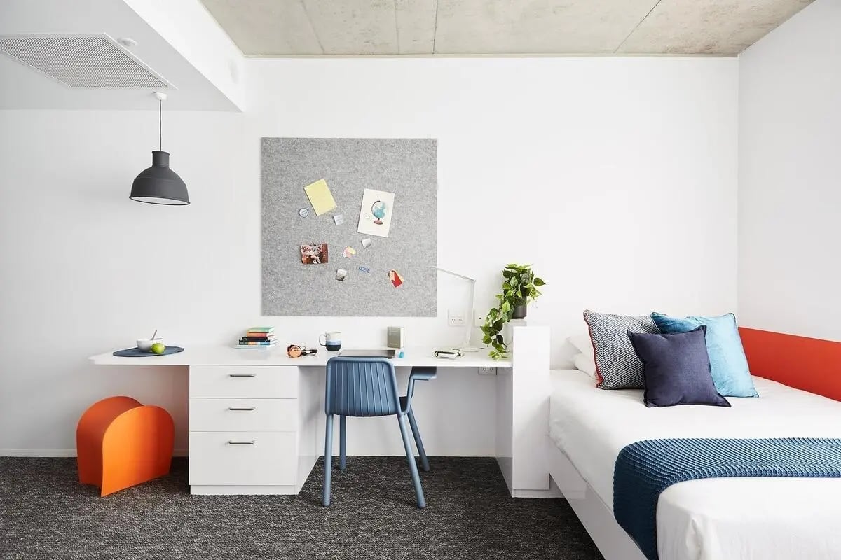 Desk bed pillows lamp plant and orange stool bedroom at Scape Toowong in Brisbane Student Accommodation