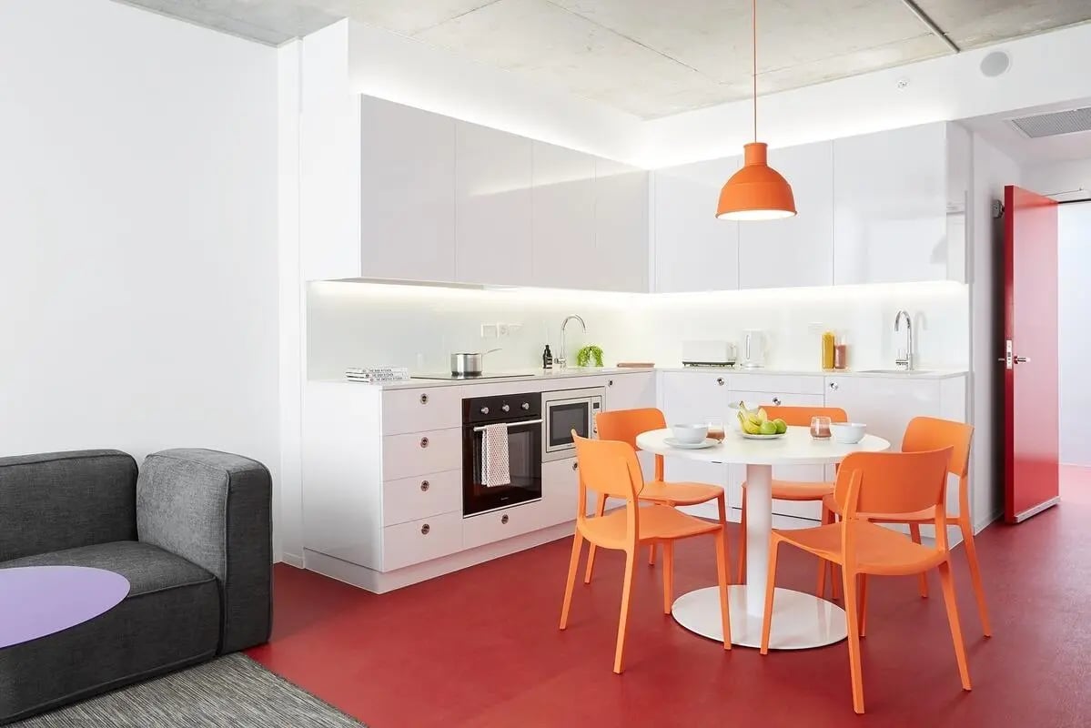 White cabinets dining table orange chairs living area kitchen at Scape Toowong in Brisbane Student Accommodation