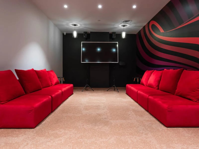 Two red sofas facing a large screen and speakers living room at Steelworks in Sheffield Student Accommodation