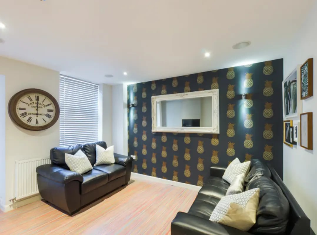 Black sofas mirror and pineapple wallpaper living room at 21 Queen Anne Street in Stoke-On-Trent Student Accommodation
