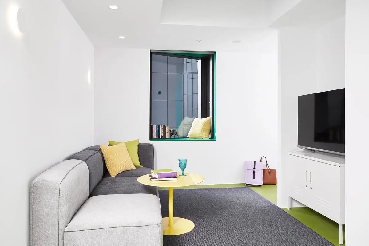 Gray sectional sofa yellow table and TV living room at Scape Carlton in Melbourne Student Accommodation