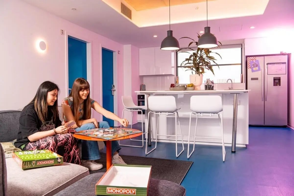 Two women playing Monopoly kitchen counter living room at Scape Carlton in Melbourne Student Accommodation