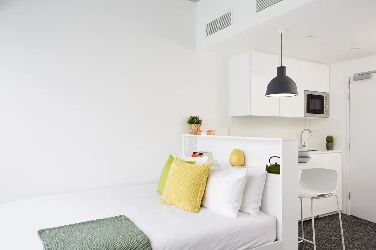 Bed pillows kitchen counter microwave white chair studio apartment at Scape Carlton in Melbourne Student Accommodation