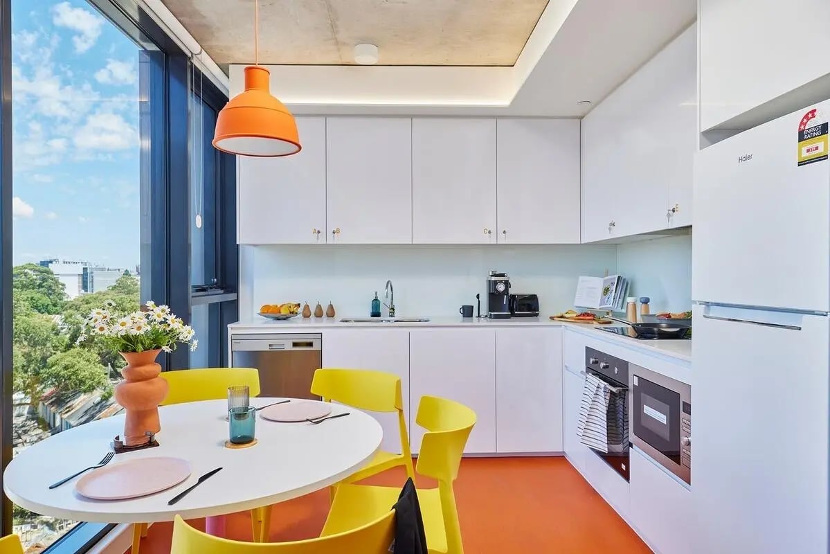 White cabinets dining table and yellow chairs kitchen at Scape Redfern in Sydney Student Accommodation