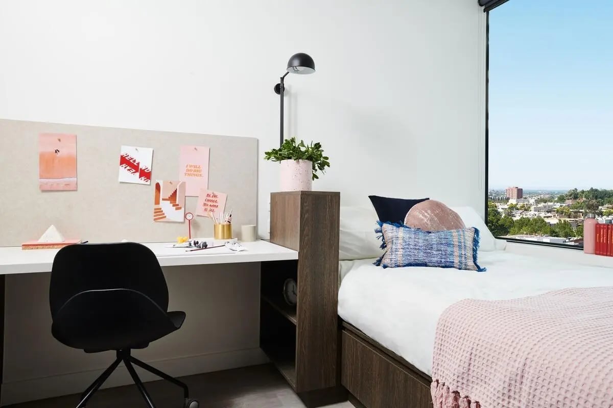 Desk bed plant pillows and cityscape Bedroom at Scape Cornell Place in Melbourne Student Accommodation