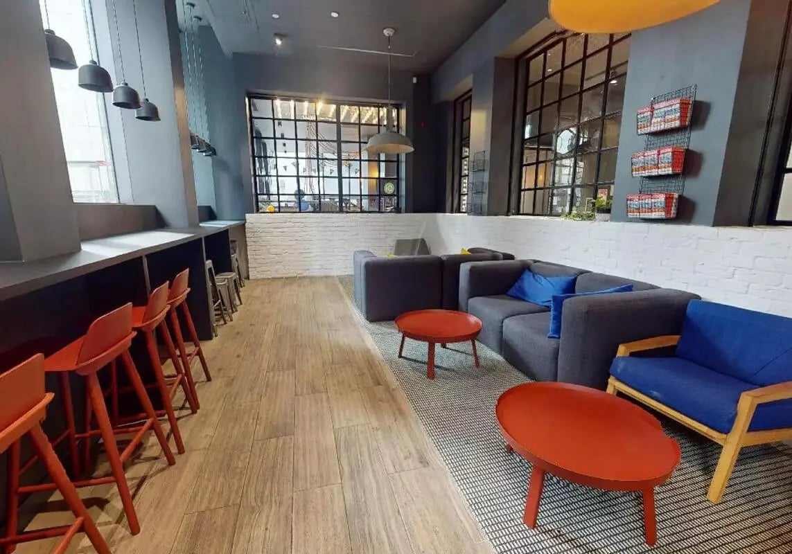 Modern lounge seating with orange stools and gray sofas Living room at iQ Shoreditch in London Student Accommodation