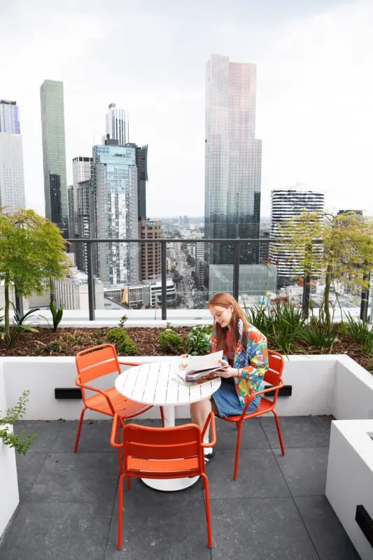 Woman reading at table outdoor patio balcony living room at Scape Victoria Street in Melbourne Student Accommodation
