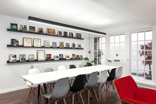 Long table and chairs with books on shelves common area at Louise House in London Student Accommodation