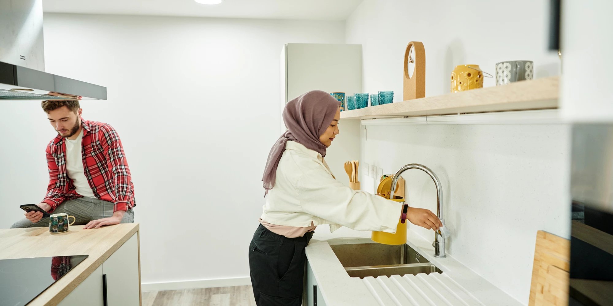 Man on phone woman at sink kitchen at Canvas Bristol in Bristol Student Accommodation