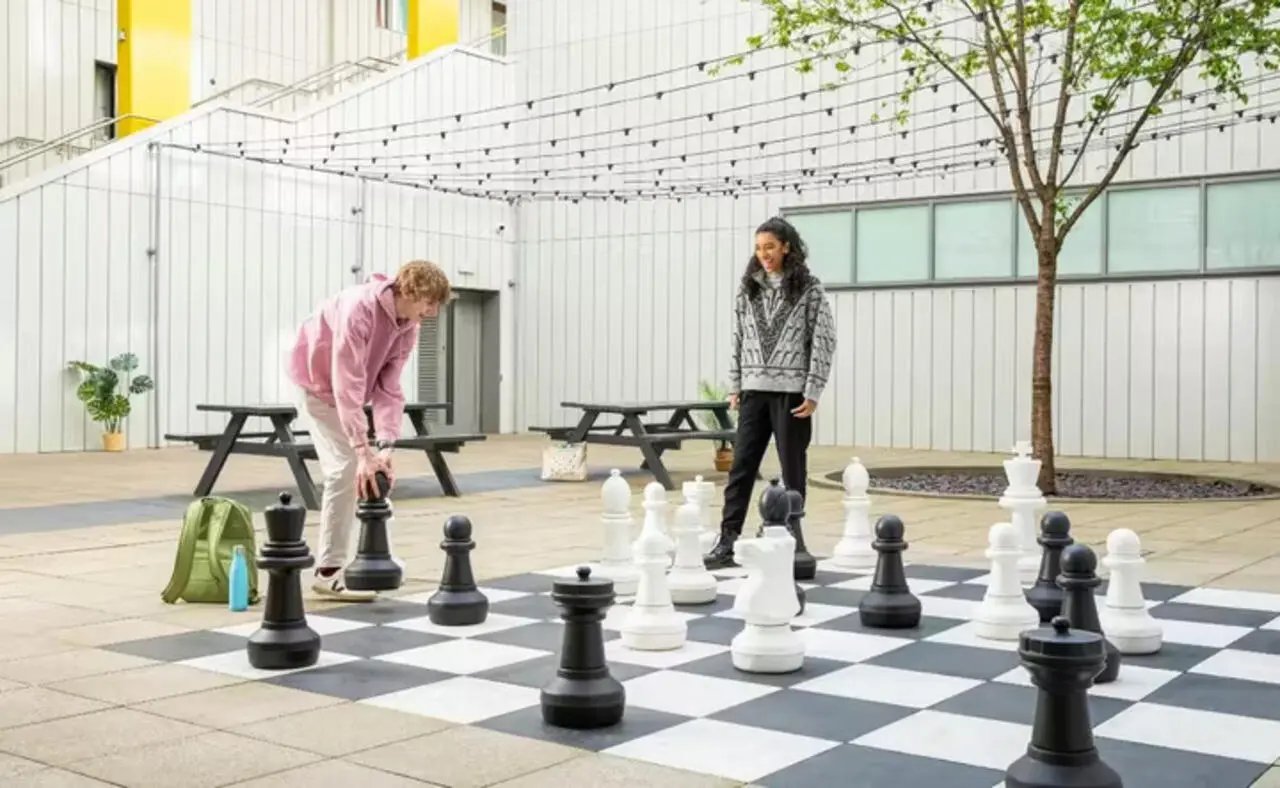Two students play giant chess outside courtyard exterior at Emily Bowes Court in London Student Accommodation