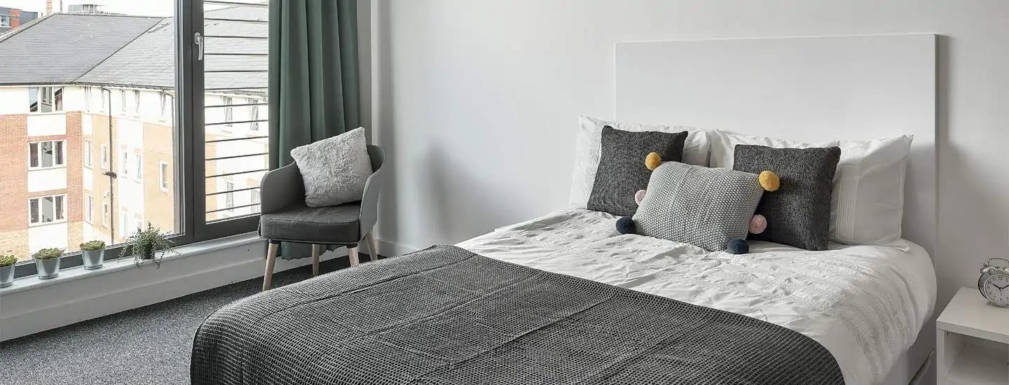 Bed with decorative pillows chair and window Bedroom at Selly Oak Apartments in Birmingham Student Accommodation