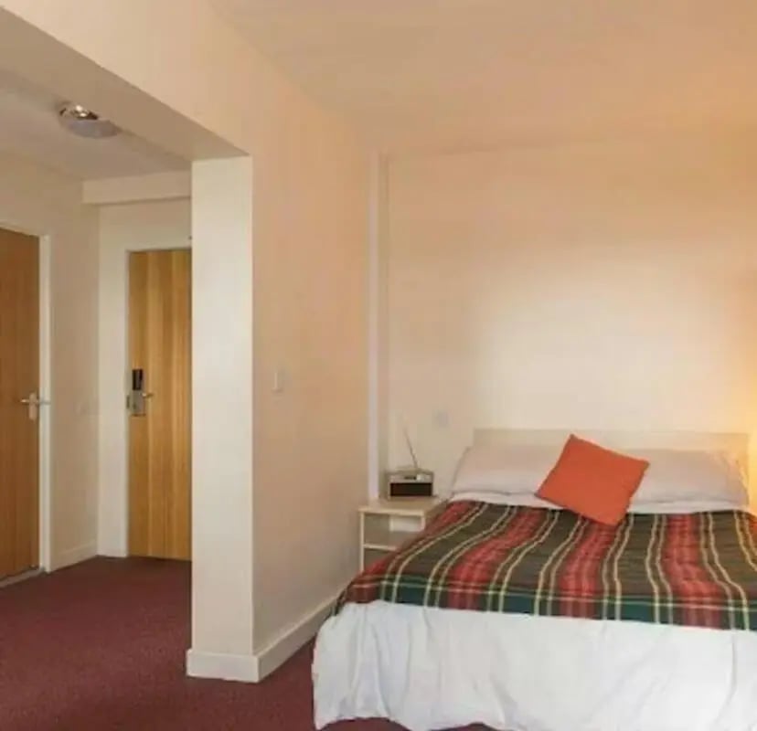 Bed with tartan blanket orange pillow bedroom at Newcastle 1 in Newcastle Upon Tyne Student Accommodation
