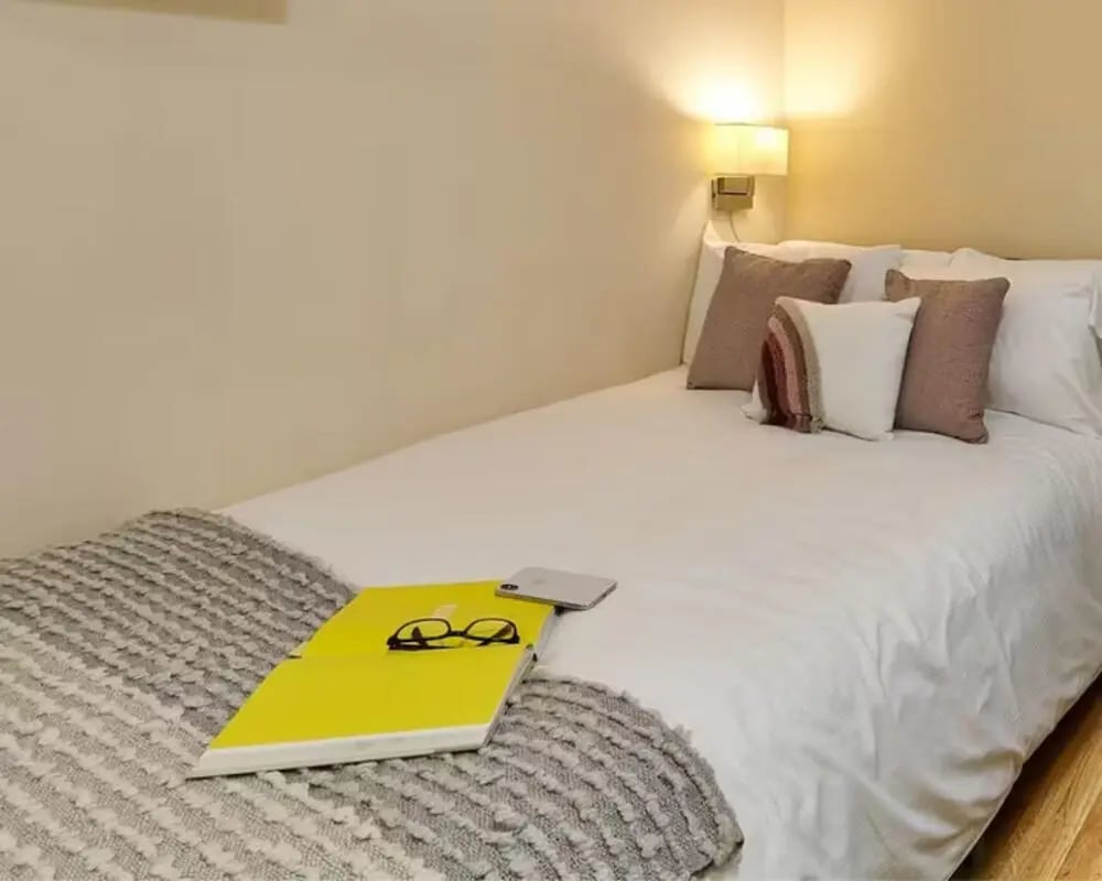 Bed with laptop glasses phone and pillows Bedroom at The Hub in London Student Accommodation