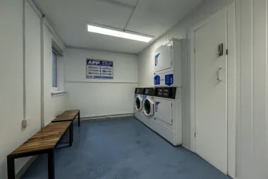 Two washing machines dryers with benches laundry room at Meadow Court in Edinburgh Student Accommodation