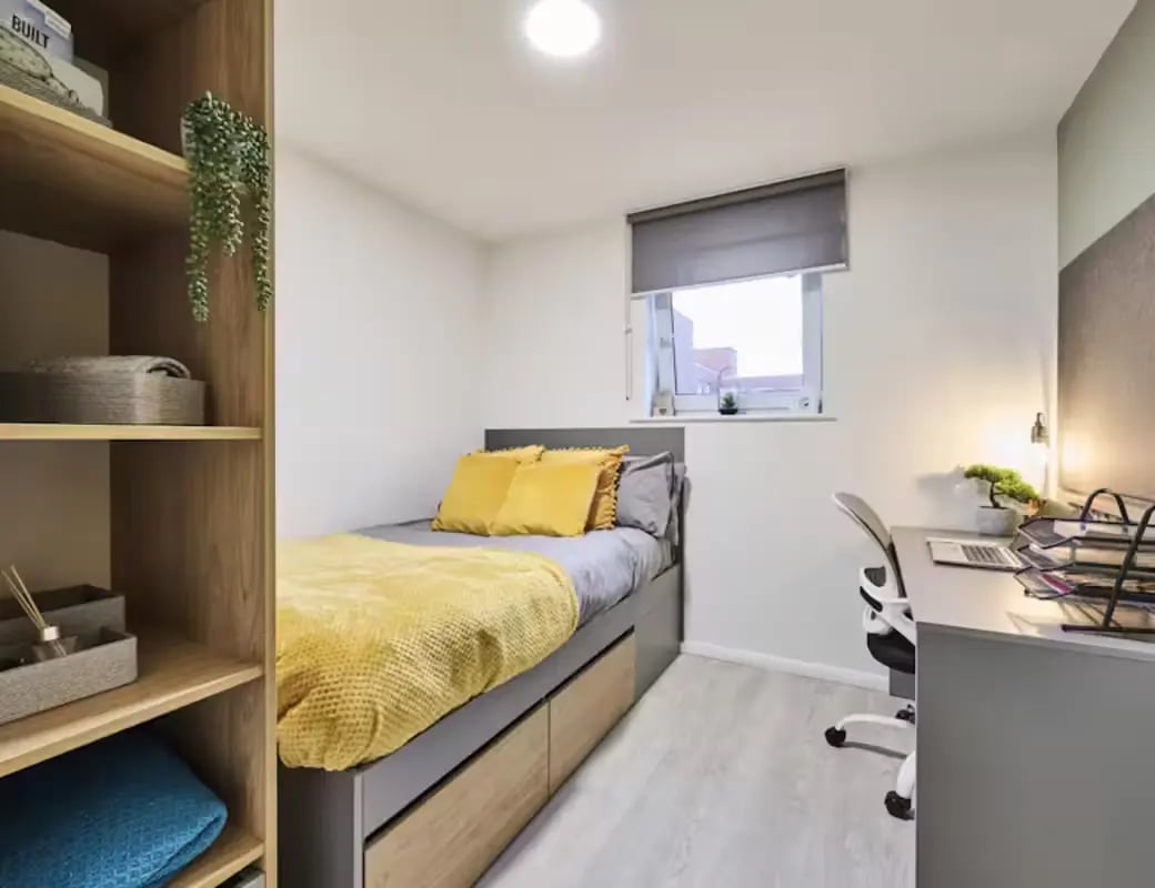 Bed with yellow bedding desk chair and shelves bedroom at Queens Court Leicester in Leicester Student Accommodation