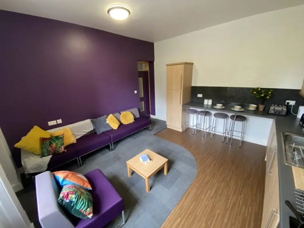 Purple couches coffee table bar stools kitchen living room at St Mary's Newcastle in Newcastle Upon Tyne Student Accommodation