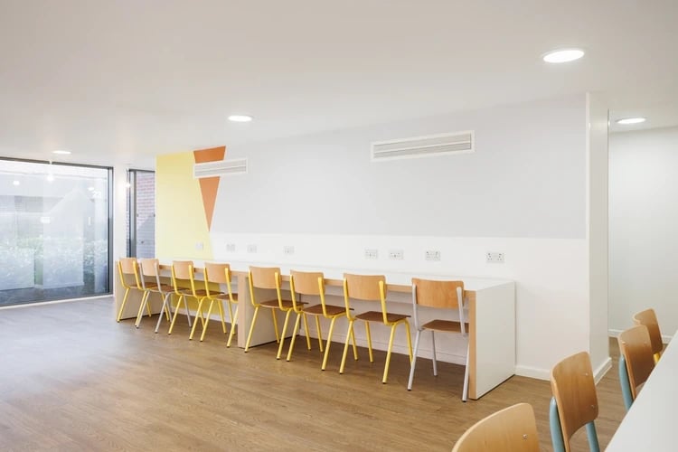 Long white desk with yellow chairs study area at St Lukes View in Liverpool Student Accommodation