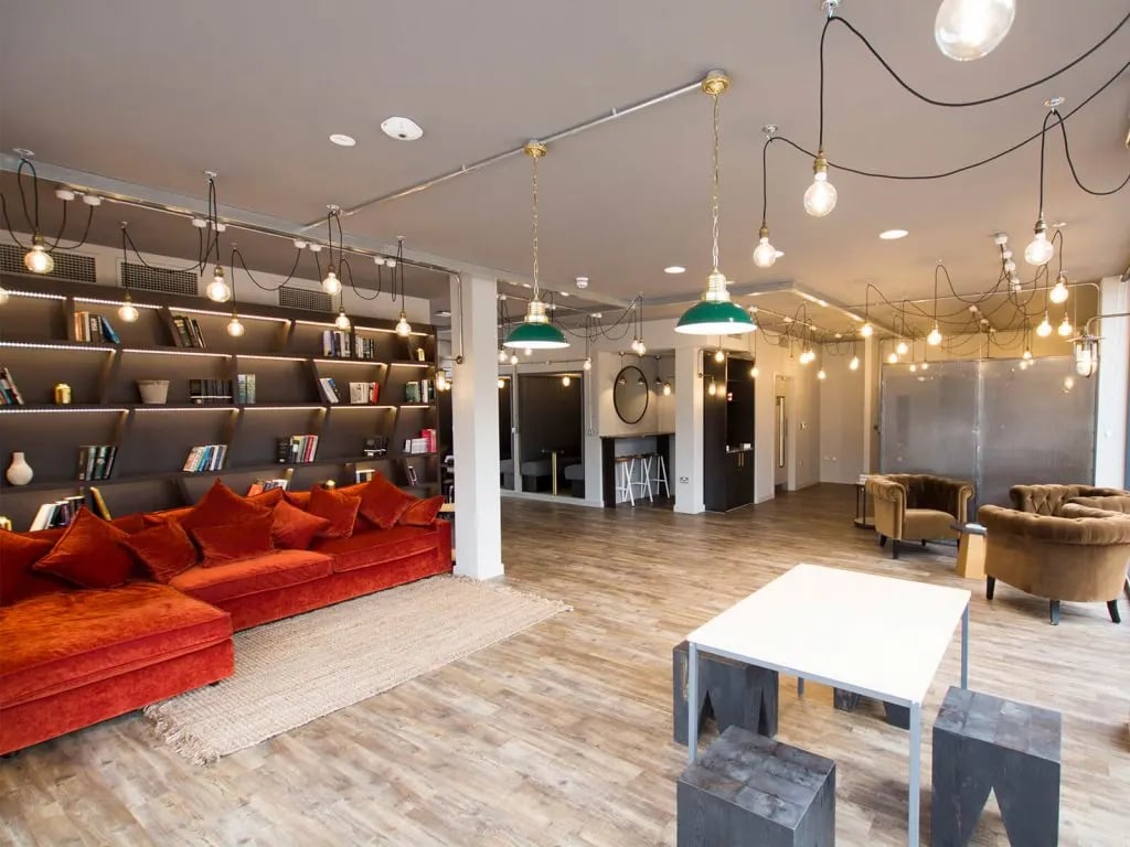 Large orange sectional sofa bookshelves and modern lighting living room at The Shield in Newcastle Upon Tyne Student Accommodation