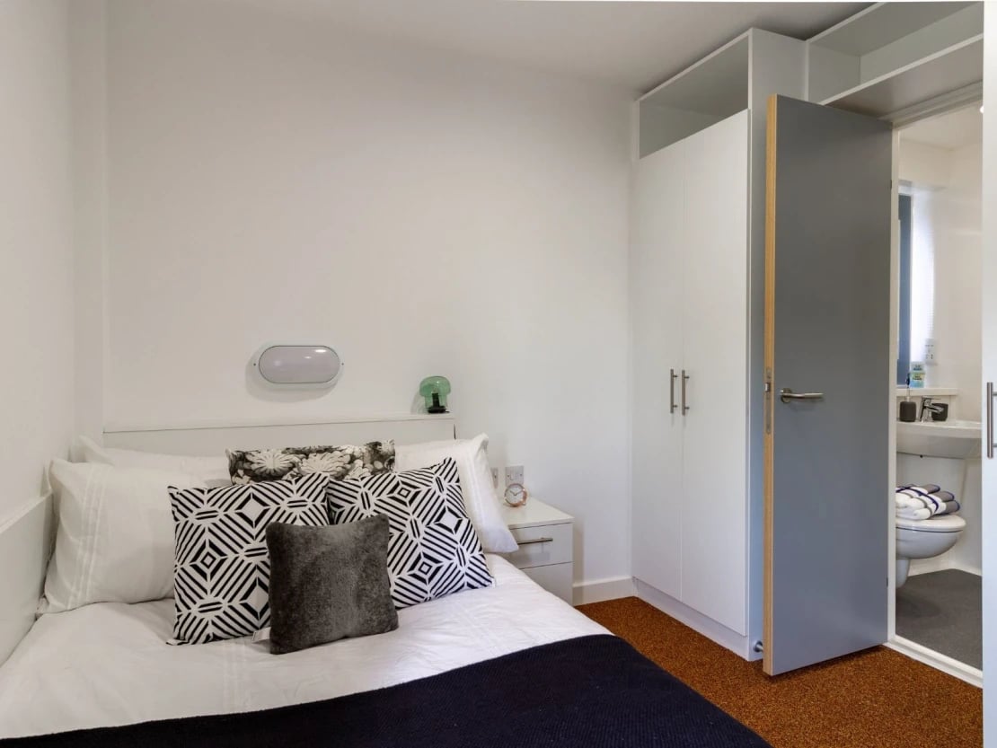 Bed with patterned pillows wardrobe and bathroom exterior at The Shield in Newcastle Upon Tyne Student Accommodation