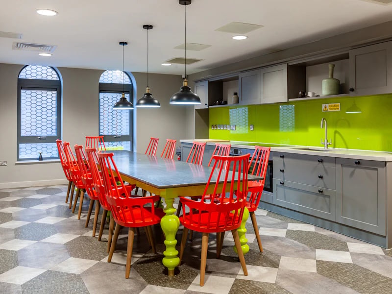 Dining table with red chairs and kitchen area kitchen at The Fitzalan in Cardiff Student Accommodation
