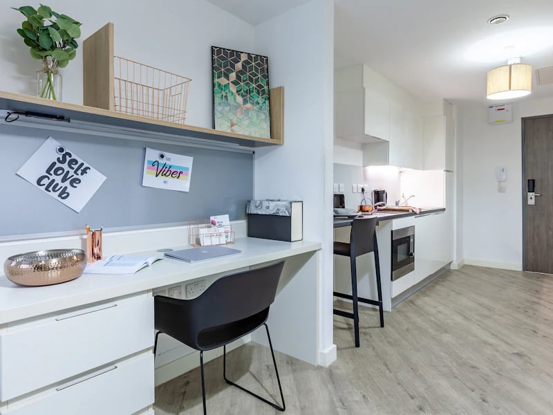 Desk with laptop and kitchen area living room at The Fitzalan in Cardiff Student Accommodation