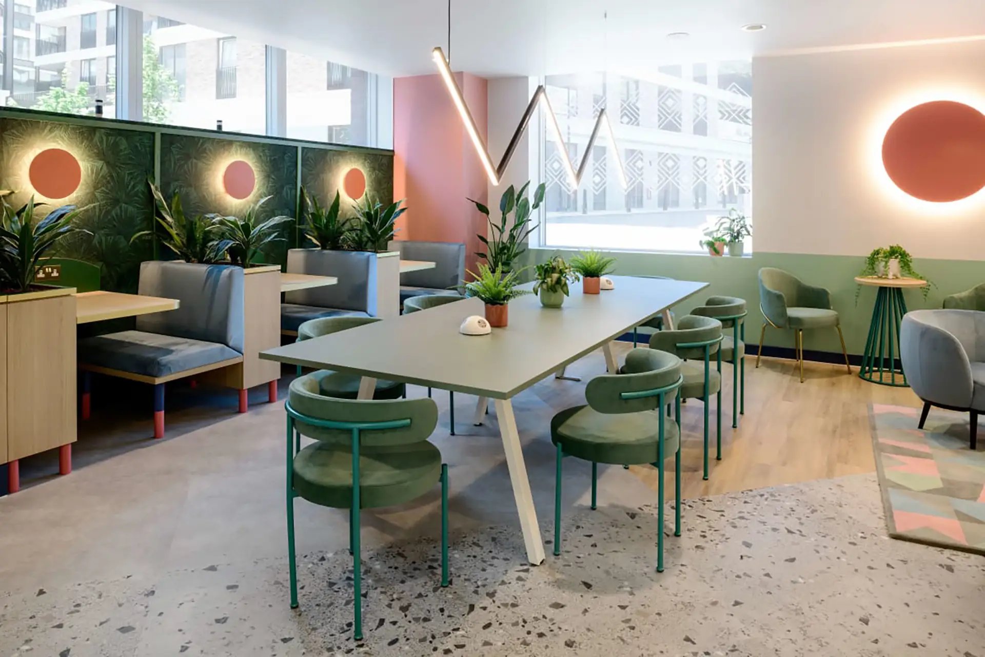 Dining table with green chairs plants and booths common area at Wick Park in London Student Accommodation