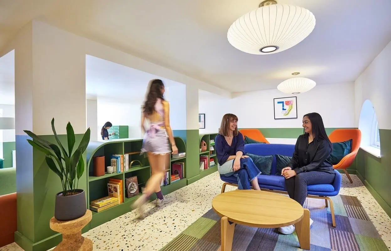Students in lounge with bookshelves sofa and plants common area at Scape Kings Cross in London Student Accommodation