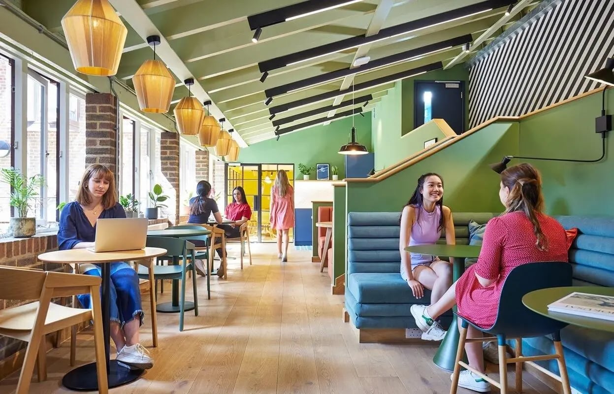 Students at tables with laptop lounge seating and staircase communal area at Scape Kings Cross in London Student Accommodation