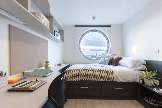 Bed desk and shelves with circular window bedroom at Livin Cardiff in Cardiff Student Accommodation