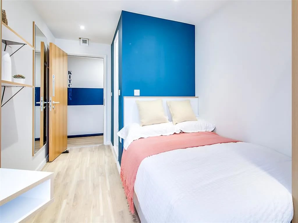 Bed with pillows coral throw and shelf bedroom at New Orient House in London Student Accommodation