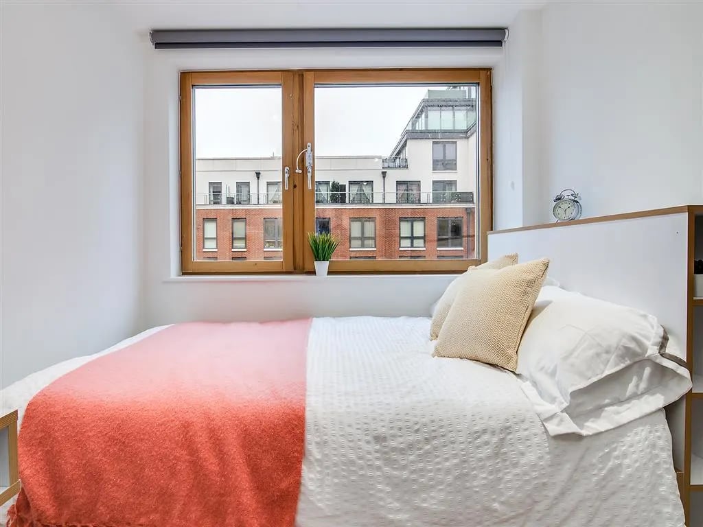 Bed with coral throw pillows and window bedroom at New Orient House in London Student Accommodation