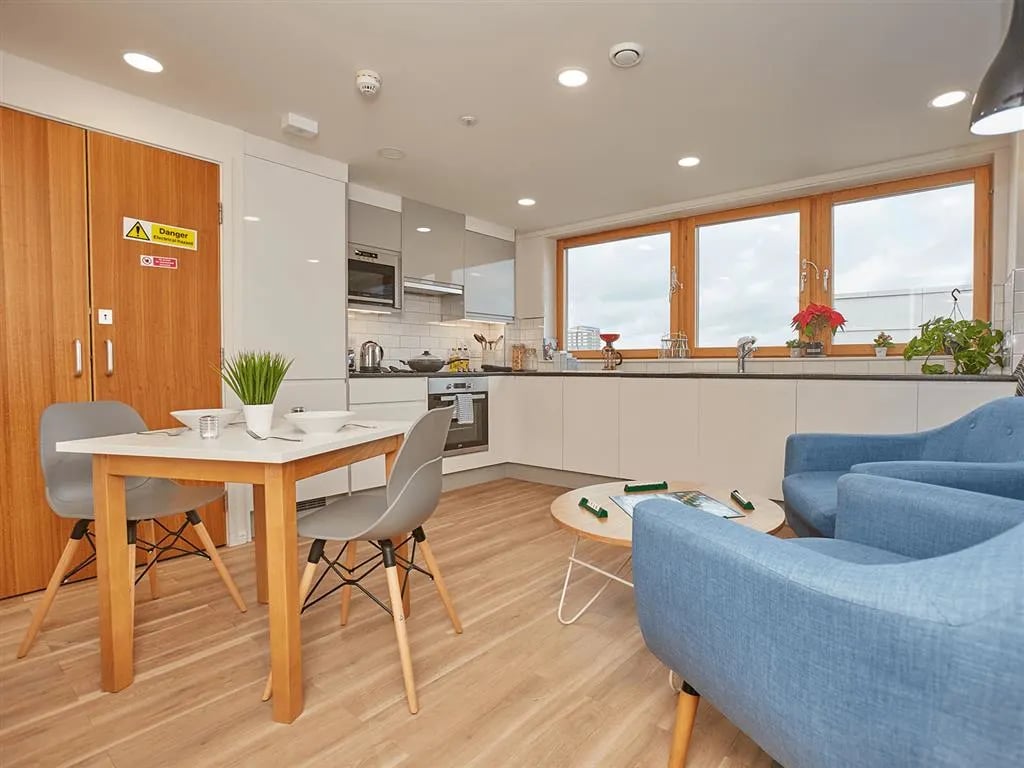 Dining table chairs blue sofas kitchen living area at New Orient House in London Student Accommodation