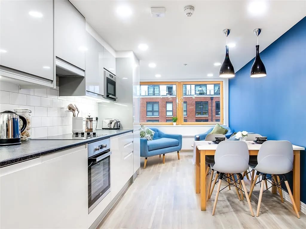 Kitchen dining area with white cabinets and blue walls living area at New Orient House in London Student Accommodation