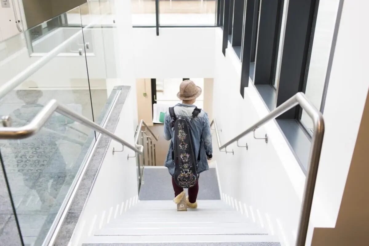 Person with musical instrument case walks down stairs Interior at Prince Consort Village in London Student Accommodation
