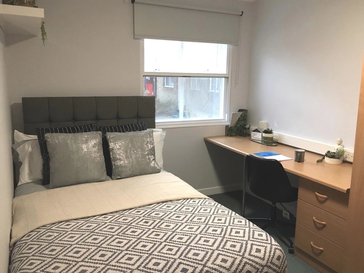 Bed with patterned duvet and desk study area bedroom at Dean House in London Student Accommodation