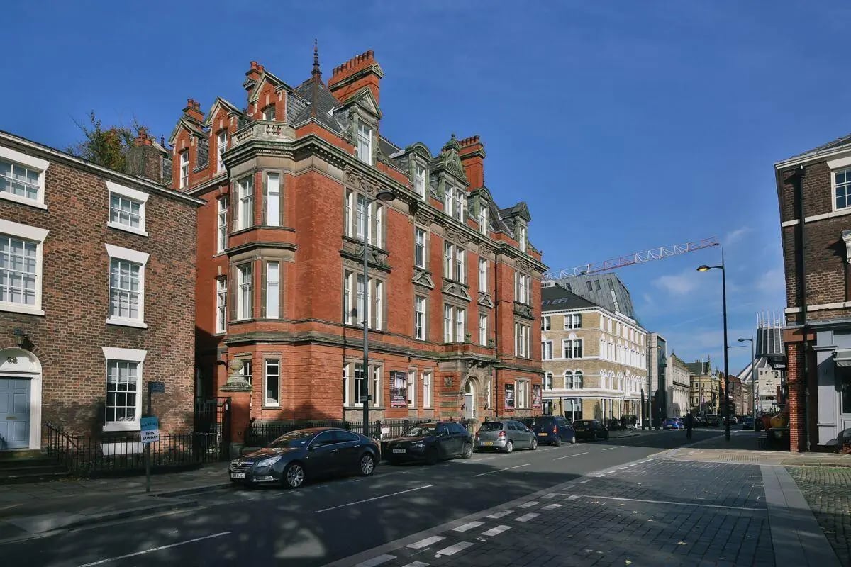 Red brick buildings with cars parked outside exterior at The Hahnemann Building in Liverpool Student Accommodation