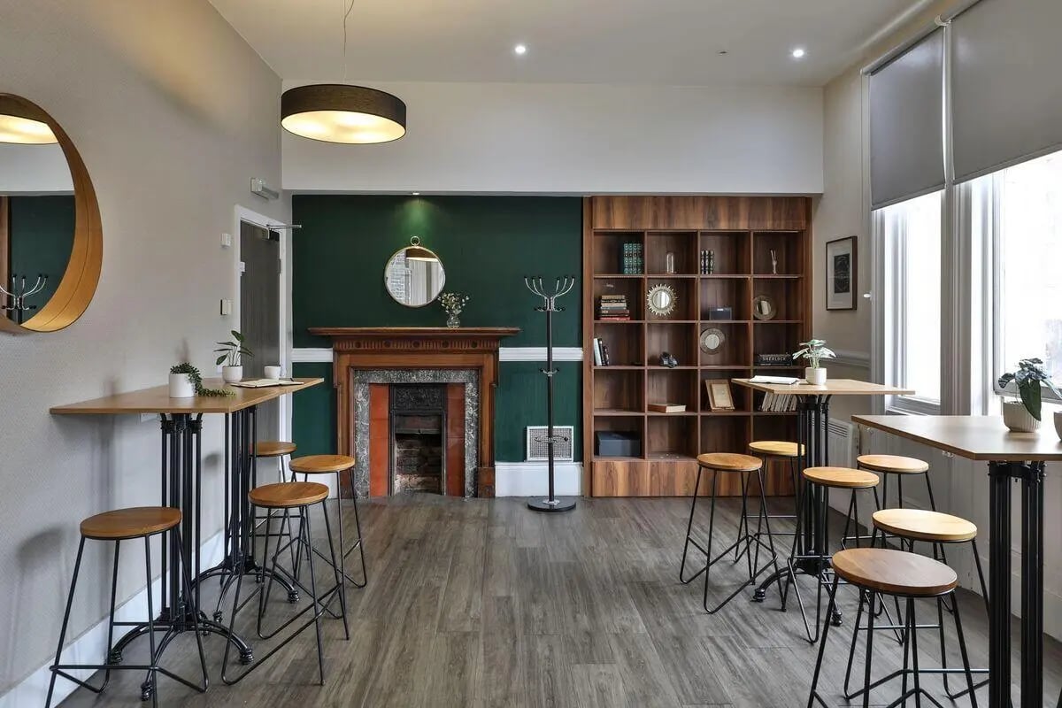Bar tables with stools by fireplace and bookshelf common area at The Hahnemann Building in Liverpool Student Accommodation