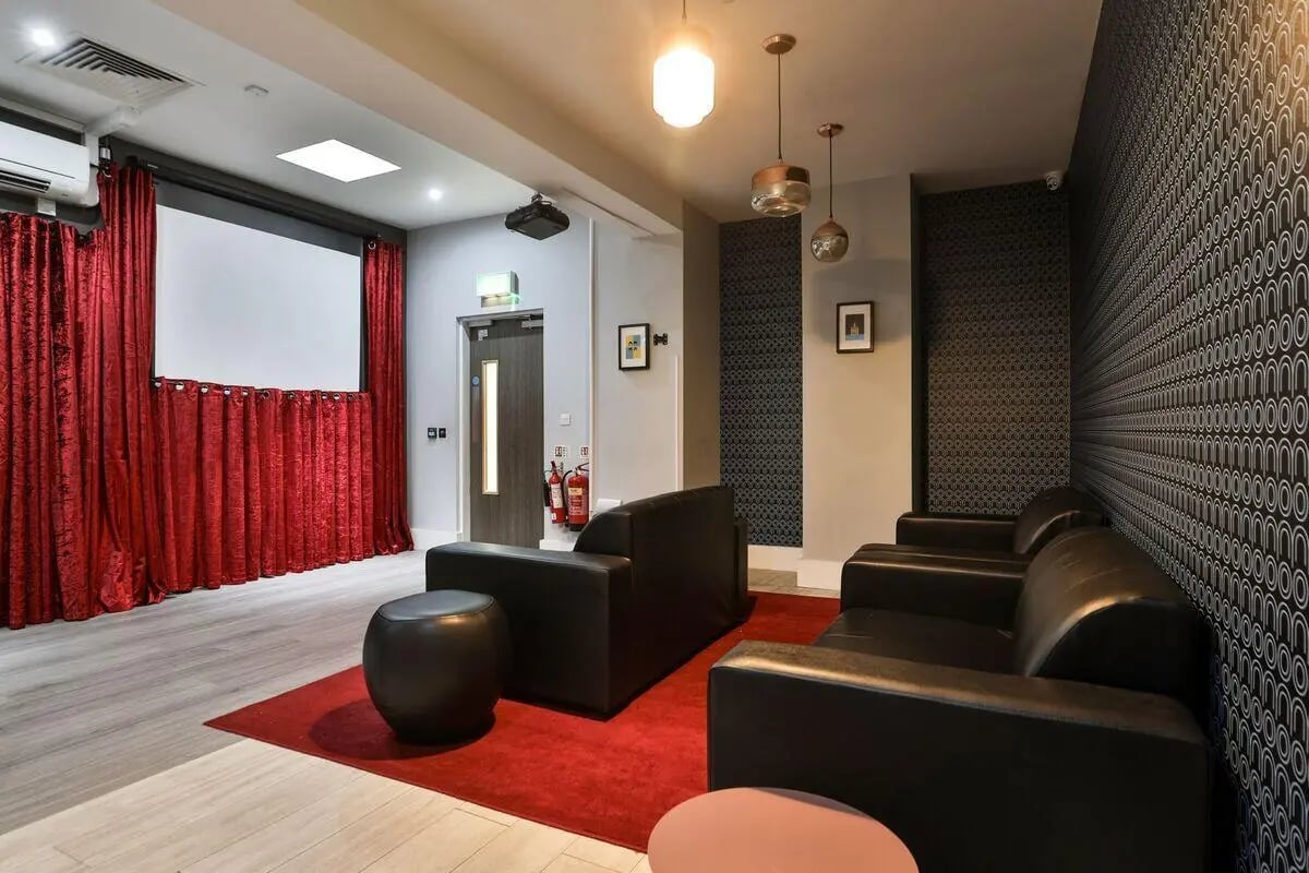 Black leather couches projector screen red curtains living room at The Hahnemann Building in Liverpool Student Accommodation