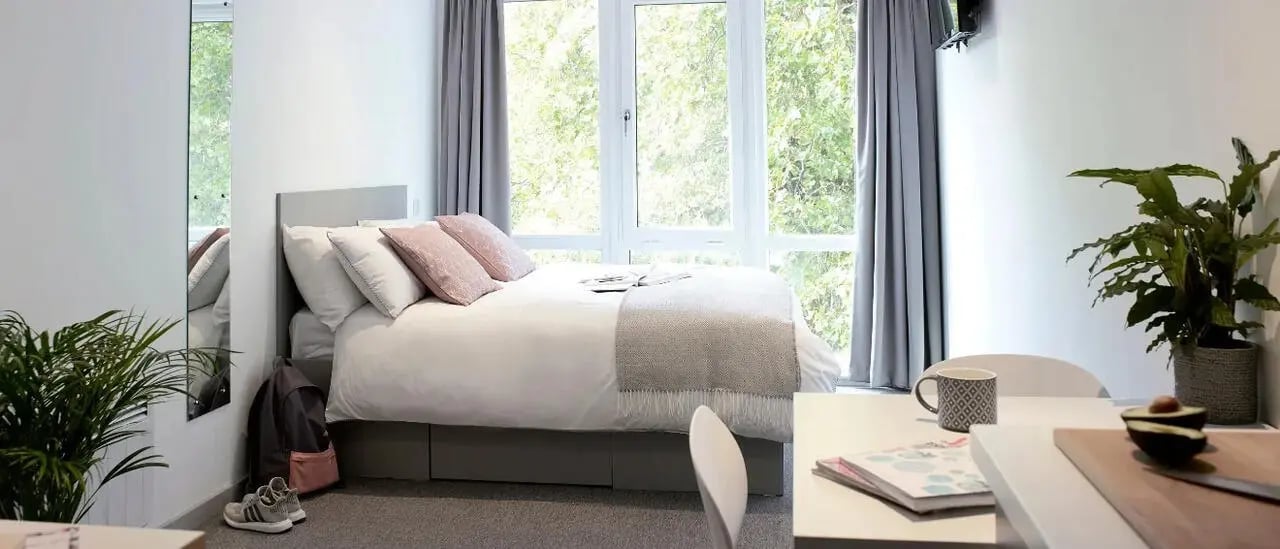 Bed with pillows plants backpack shoes and desk bedroom at Lace Market Studios in Nottingham Student Accommodation