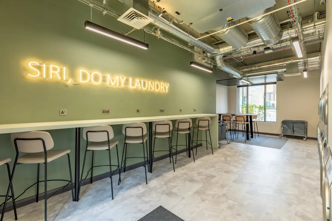 Bar stools along counter with neon sign laundry room at Winfield Court in Nottingham Student Accommodation
