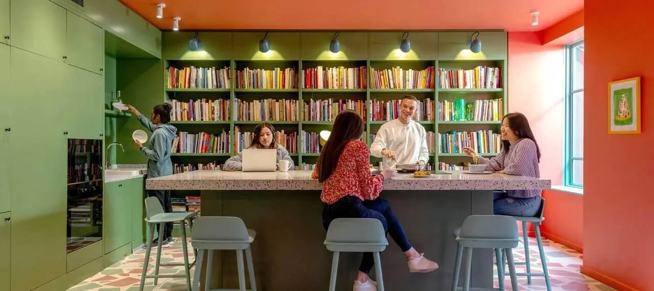 Students by bookshelves and kitchen common area at Scape Bloomsbury in London Student Accommodation