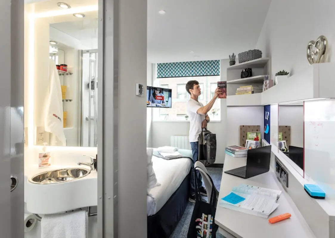 Student puts book on shelf with desk bedroom at Brotherton House in Leeds Student Accommodation