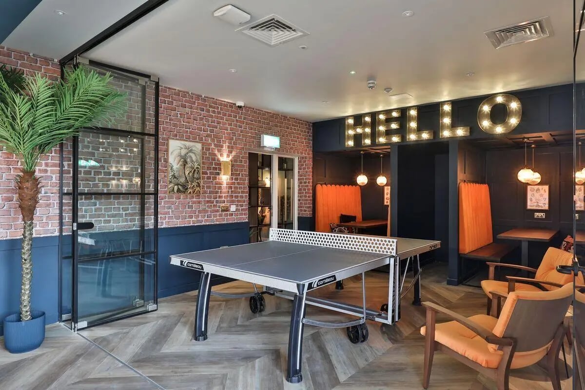 Ping pong table chairs booths and hello sign common area at St Mary's in Bristol Student Accommodation