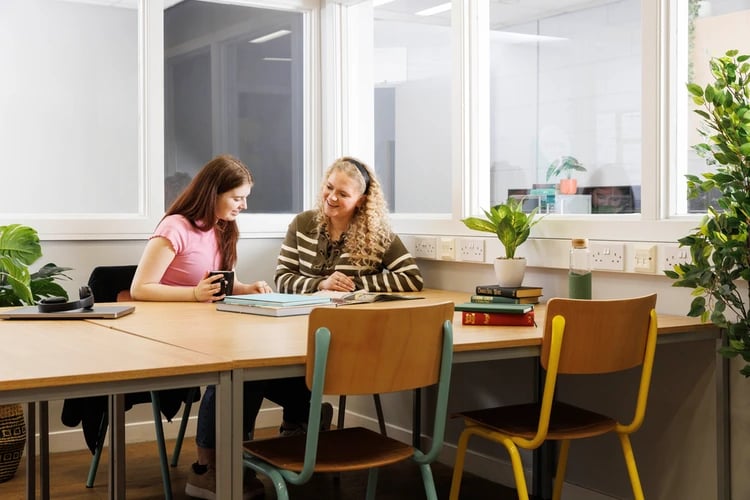 Two students study at wooden table with chairs and plants study area at Spring Gardens in Aberdeen Student Accommodation