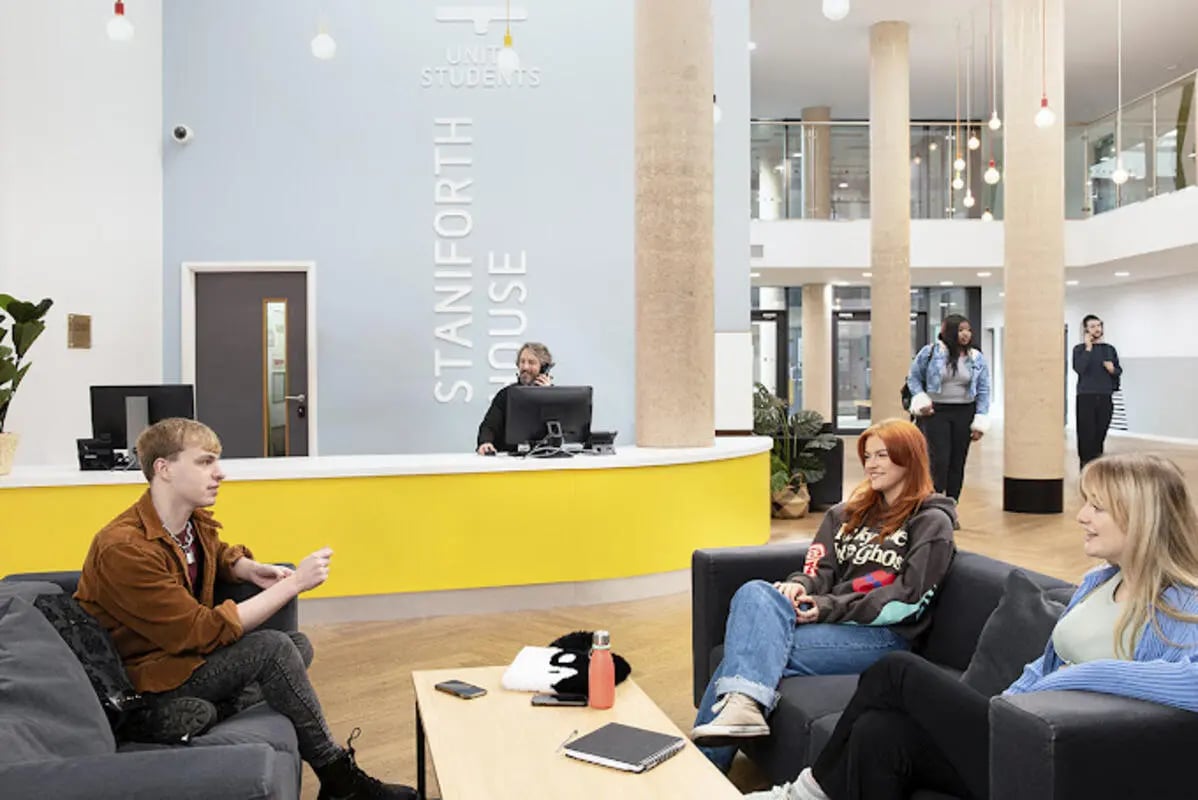 Students sit on couches by yellow reception area communal space at Staniforth House in Birmingham Student Accommodation