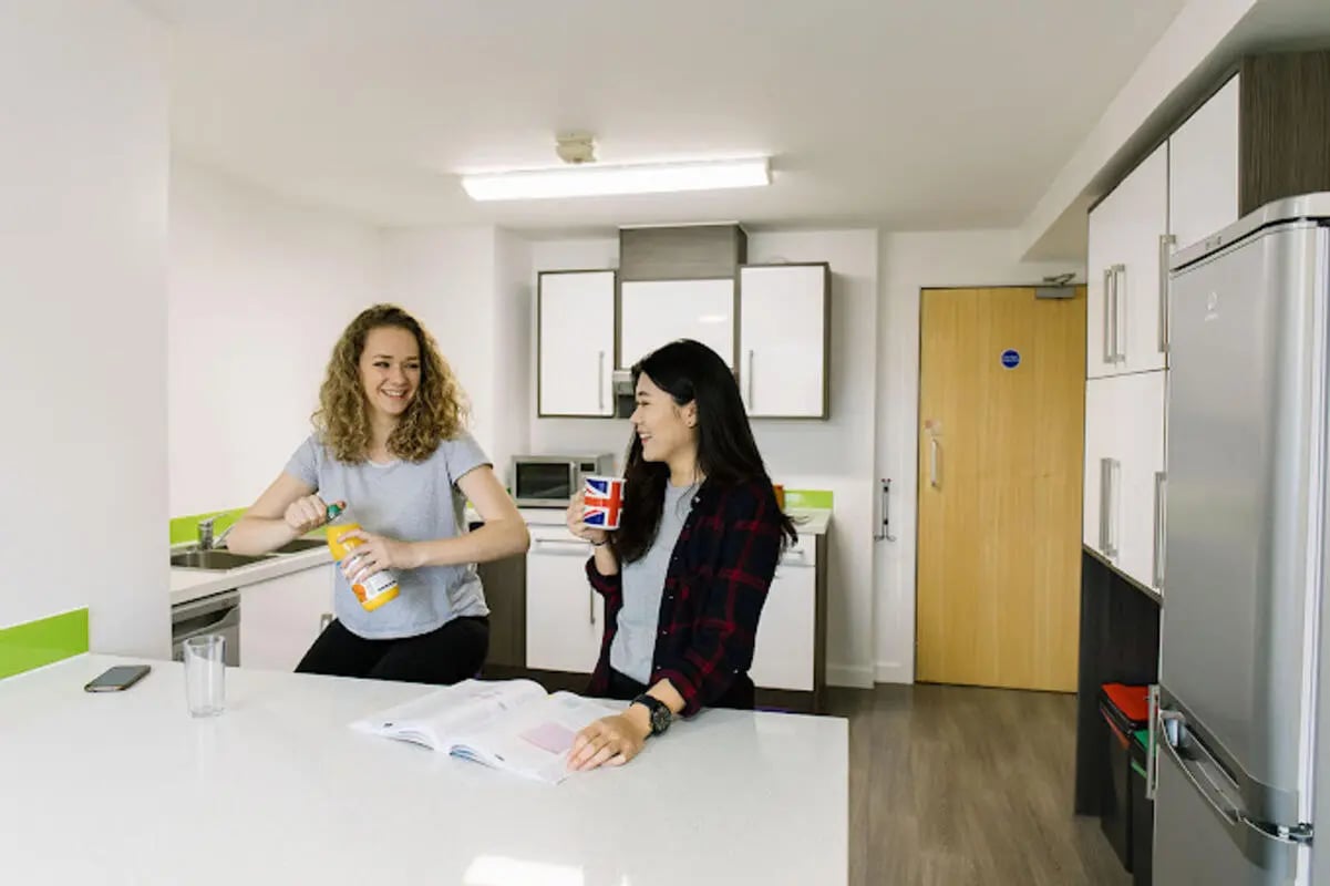 Two women with drinks in a modern kitchen at Queen's Park House in Coventry Student Accommodation